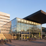 Das Eingangsgebäude karo 5 (S1|01) der TU Darmstadt am Karolinenplatz. Das 2009 fertiggestellte Gebäude ist Teil des Universitätszentrums und umfasst ein Studierenden-Informations-Service, eine Cafébar sowie ein Ausstellungs- und Aufenthaltsbereich. Im Hintergrund links ist das Verwaltungsgebäude, erbaut in den 1970er Jahren, zu sehen. Bild aufgenommem im März 2016.